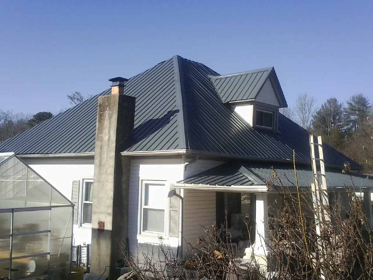 Dark blue standing seam metal roof on a white farmhouse with dormer — Slate & Tile Roof Repair by Roofing Brothers in Oak Ridge