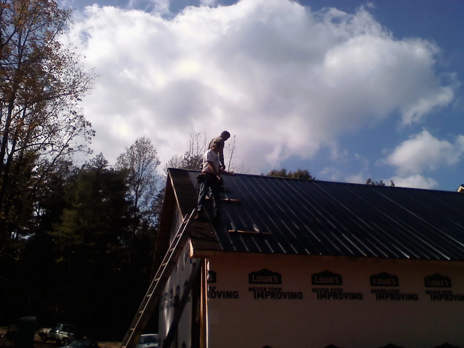 Roofer fastening dark metal panels high against a cloudy sky, from a Roof Inspection job in Oak Ridge