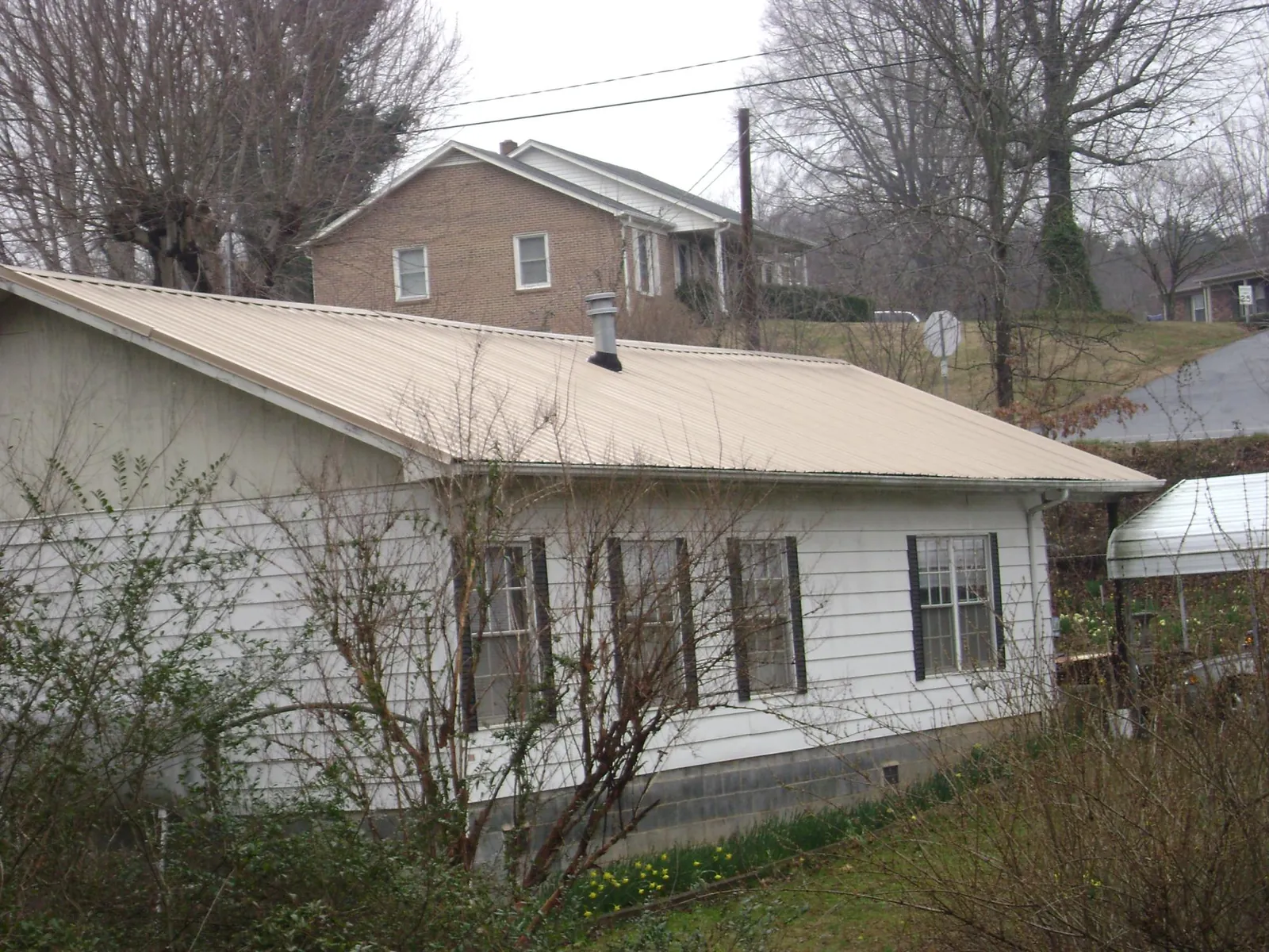Tan metal roof on a white sided house set into a hillside — Commercial Roofing by Roofing Brothers in Oak Ridge