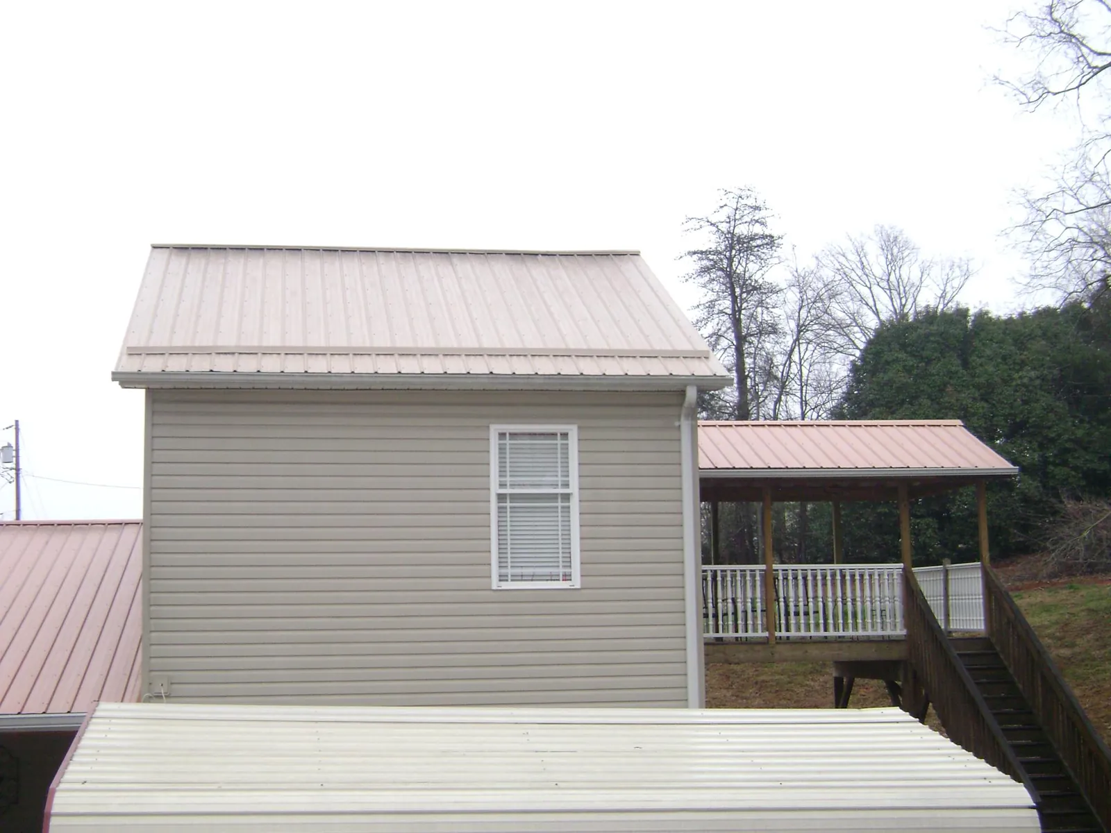 Tan metal roofs on a two story addition and attached porch, from a Roof Replacement job in Oak Ridge